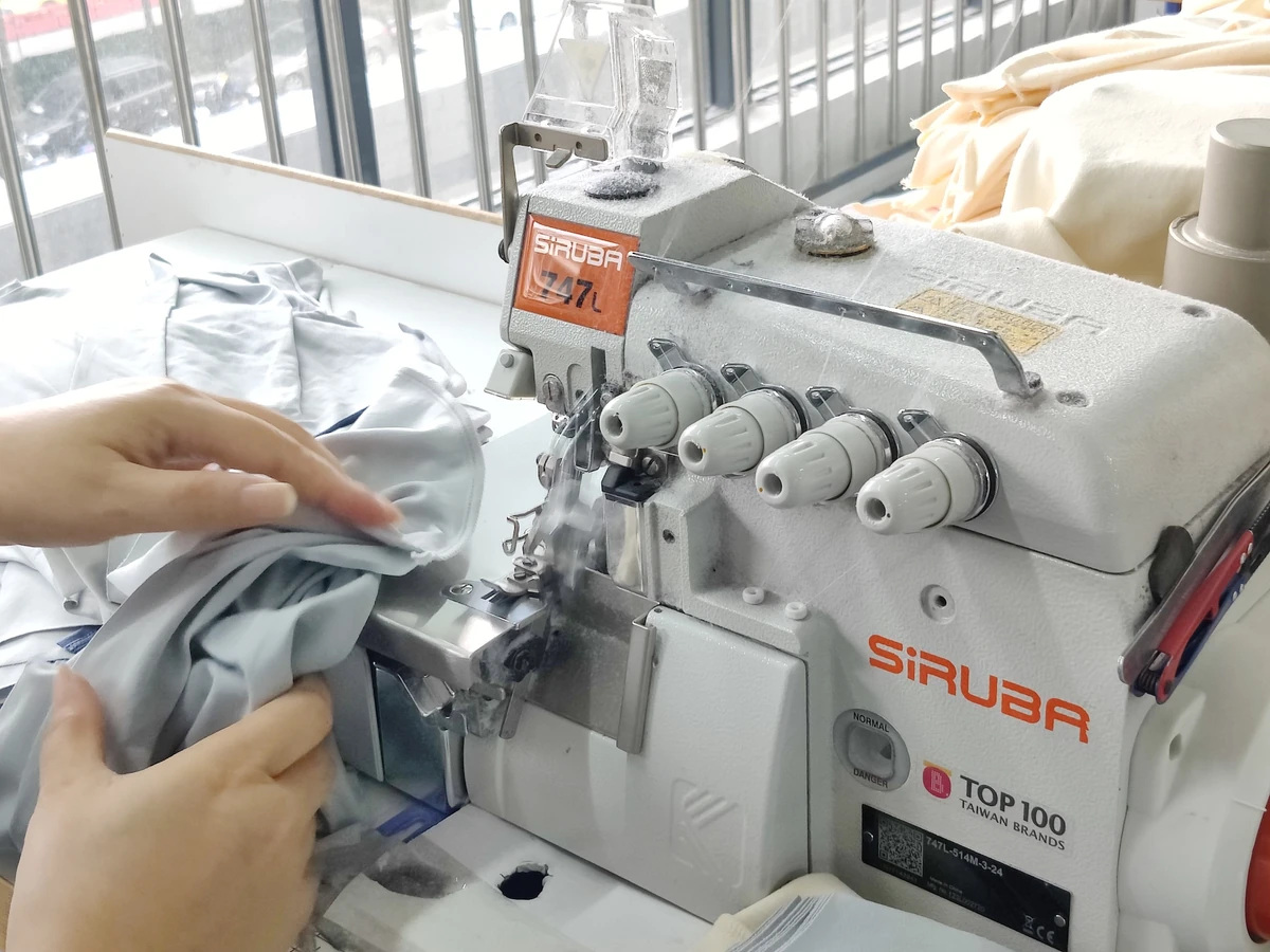 Close-up of an overlock sewing machine finishing a seam on knit fabric with the operator guiding the edge